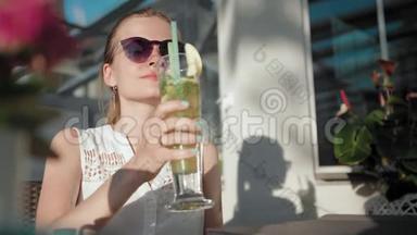戴墨镜的女商人在夏天的咖啡馆里用吸管喝鸡尾酒